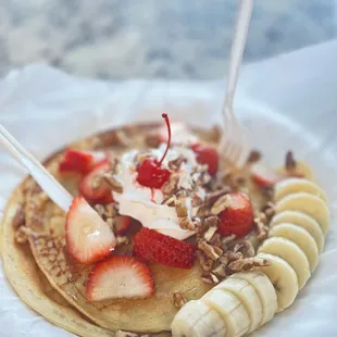 a plate of pancakes with strawberries, bananas, and nuts