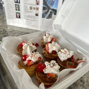 a container of donuts with whipped cream and strawberries