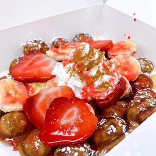 Vanilla Bubble Waffle with strawberry drizzle, fresh strawberries, bananas, whip, cinnamon, maple syrup and powdered sugar