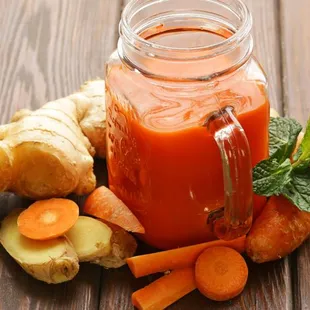a jar of carrot juice surrounded by fresh vegetables