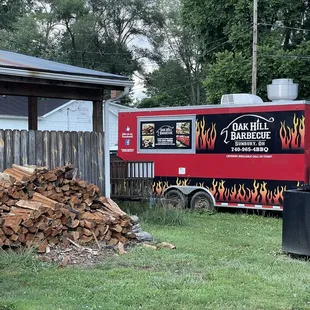 a red food truck parked next to a pile of wood
