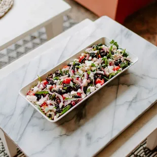 a salad on a white platter on a marble coffee table