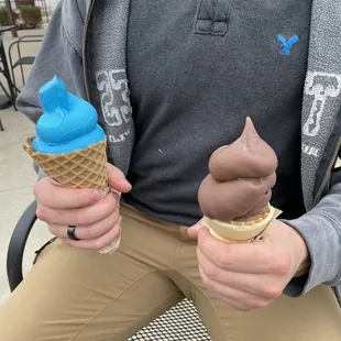 Blue cookies and cream ice cream in a waffle cone and a chocolate ice cream in a regular cone