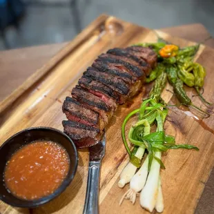 a steak on a cutting board with a side of salsa