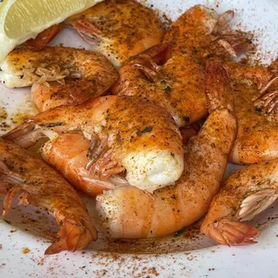 a plate of cooked shrimp with a lemon wedge