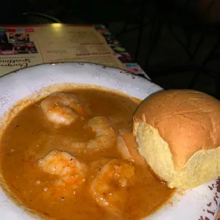a plate of shrimp soup with a roll