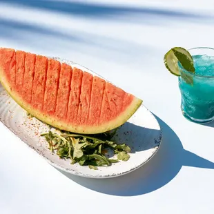 a slice of watermelon on a plate next to a glass of watermelon