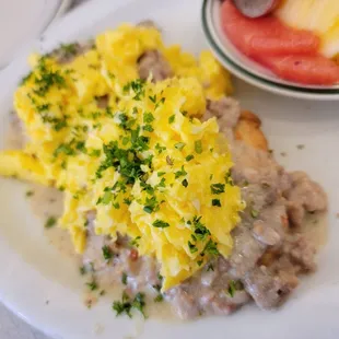 a plate of eggs, sausage, and fruit
