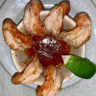 a plate of shrimp with ketchup and a lime