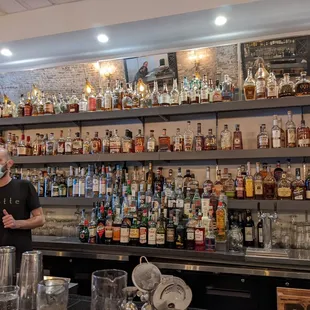 a man standing behind a bar filled with bottles of alcohol