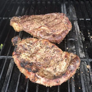 two steaks cooking on a grill
