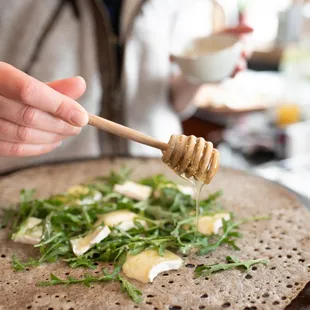a person holding a wooden spoon over a pizza