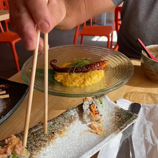 a person holding chopsticks over a plate of sushi