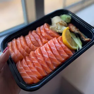 a person holding a tray of salmon