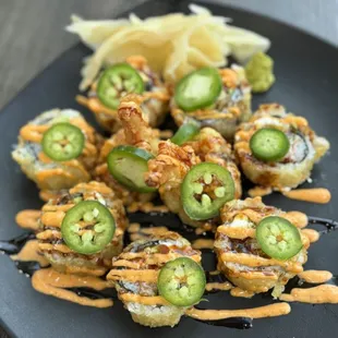 a plate of sushi rolls with sauce and jalapenos