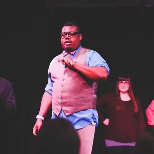 a man in a vest and tie standing in front of a group of people