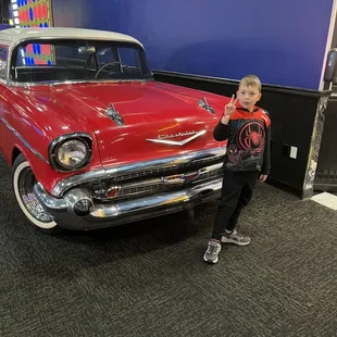 a young boy standing in front of a classic car