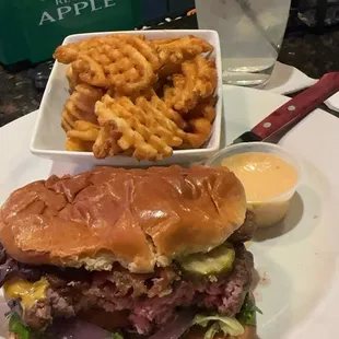 Bacon cheeseburger cooked, medium rare with waffle fries and a side of chipotle sauce... with a bite or two taken out of it already