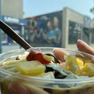 a hand holding a cup of fruit and yogurt