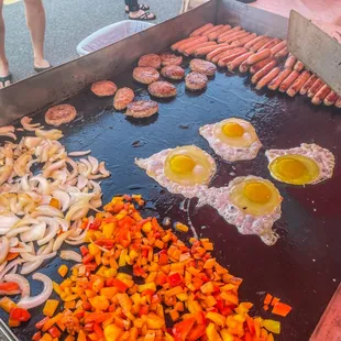a grill with sausages, eggs, and peppers