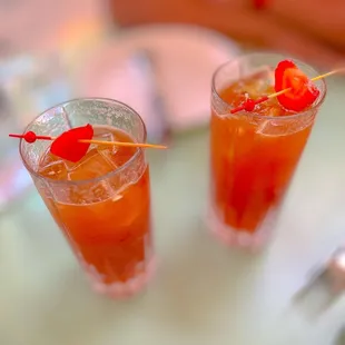 two glasses of orange juice with a cherry garnish