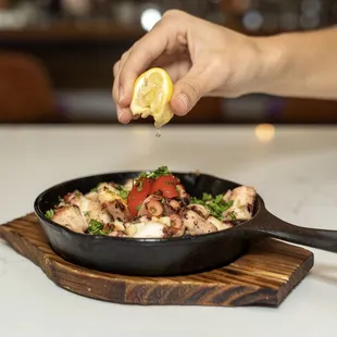 Squeezing Lemon onto Polvo Grelhado Appetizer - Sizzling Sauteed Octopus in Garlic Sauce