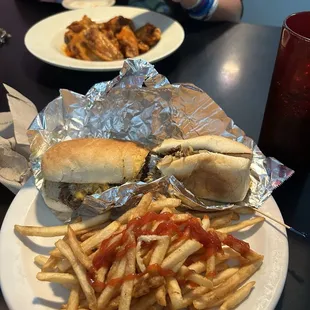 On the far side it is hot chicken wings and on the front plate French fries with a Philadelphia cheesesteak sandwich.