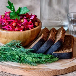 a wooden plate with bread, salad, and a glass of water