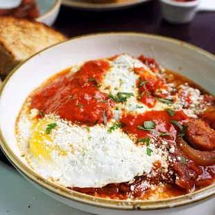 Shakshuka: two sunny up eggs, stewed San Marzano tomatoes, onions, peppers, cotija, harissa, grilled bread ($16). Add sausage ($2).