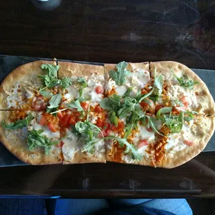a flatbread pizza with cheese, tomatoes, and arugula