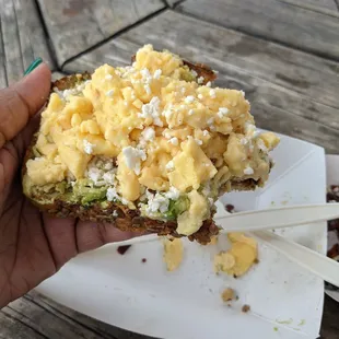 a hand holding a piece of bread with eggs on it