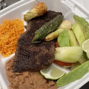 Carne Asada A La Mexicana served with grilled onions, grilled jalapeño, avocado, tomato cucumber salad, and rice and beans