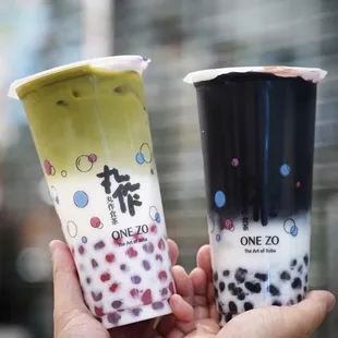 a hand holding two cups of bubble tea