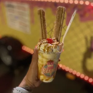 a hand holding a cup of ice cream and pretzels