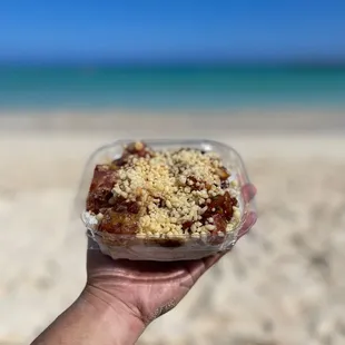 a hand holding a container of food on the beach