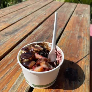 a bowl of ice cream and fruit on a picnic table