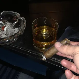 a hand holding a cigar and a glass of whiskey