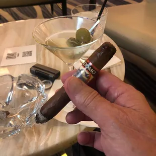 a hand holding a cigar and a glass of martini