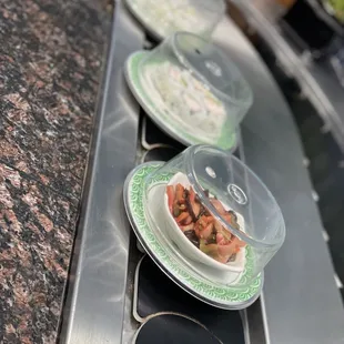 three plates of rice sushi on a conveyor belt
