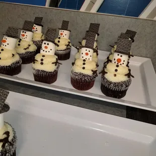 a tray of cupcakes with frosting snowmen