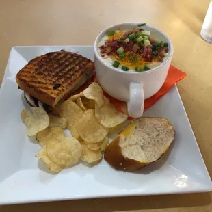 A cup of loaded baked potato soup. Along with half of a grilled portobello mushroom sandwich .