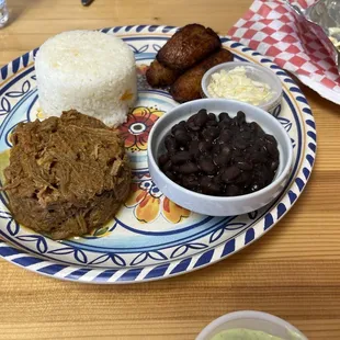 The plate with rice, black beans, shredded beef, plantains, and cheese.