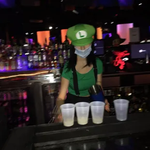 a woman wearing a mask and a green hat behind a bar
