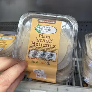 a hand holding a package of hummus