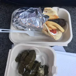 a hot dog and a stuffed grape leaves in a styrofoam container