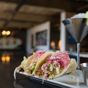 two tacos on a plate with a martini in the background