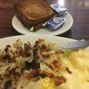 Scrambled eggs American cheese on top of eggs, Hashbrowns with onions and wheat toast also included is coffee.