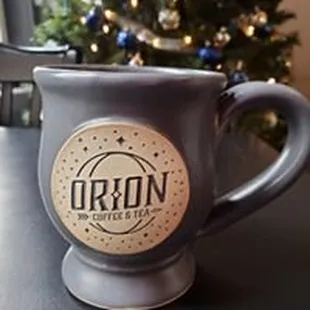 a coffee mug on a table with a christmas tree in the background