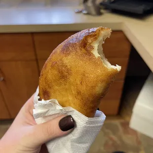 a hand holding a pastry with a bite taken out of it