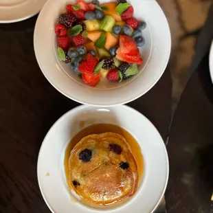 two plates of pancakes and a bowl of fruit